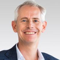 Mid-close up of The Hon Andrew Giles MP smiling in front of a light background